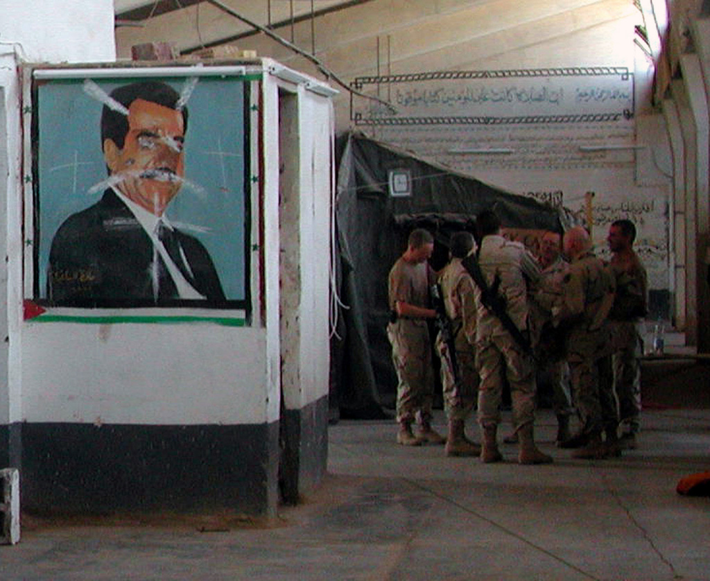 US Army (USA) Soldiers confer near a defaced mural of Saddam Hussein at the Baghdad Central Detention Facility, formerly the Abu Ghraib Prison, in Baghdad, Iraq (IRQ). (SUBSTANDARD)